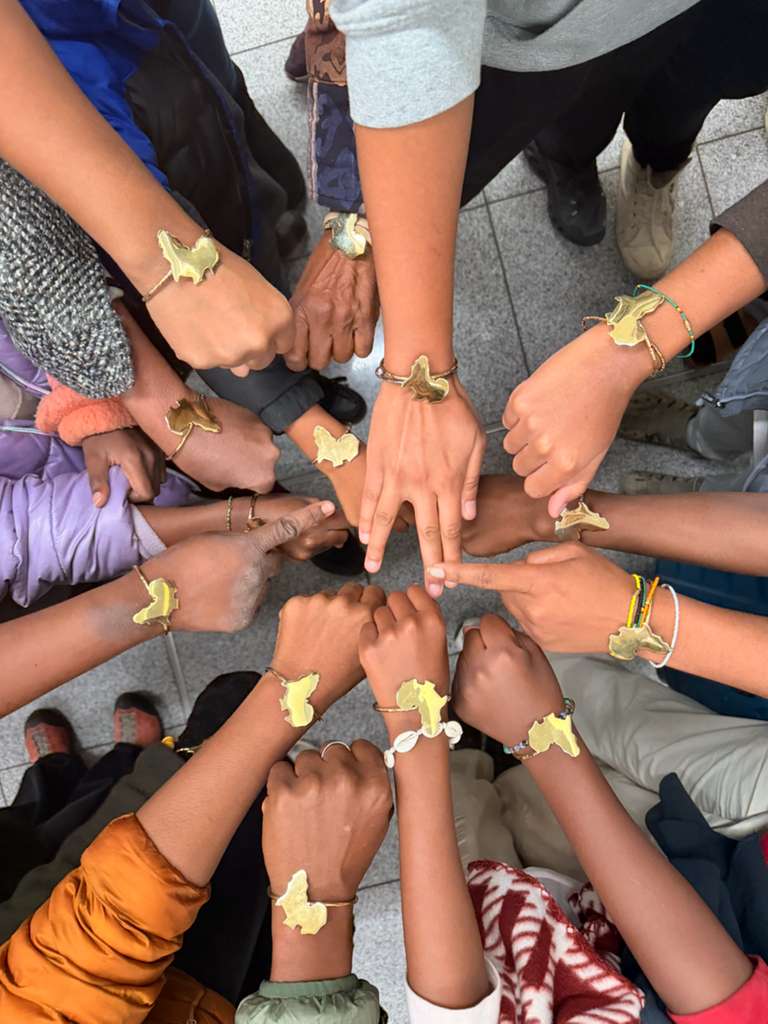Youth circle of hands wearing brass Africa-shaped bracelets